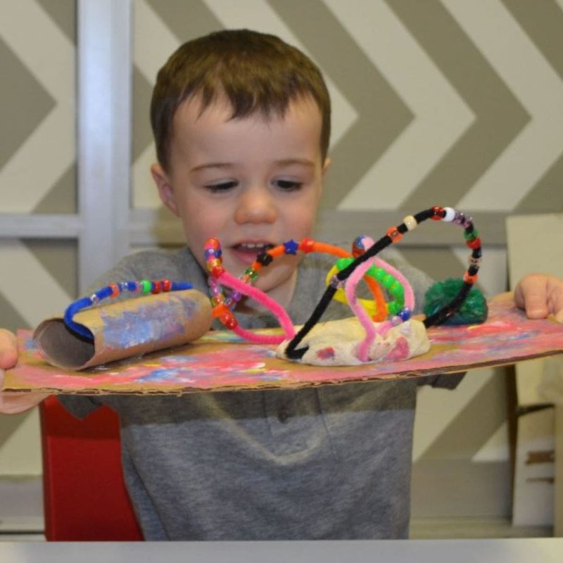 nursery school student presenting his project made out of clay, pipe cleaners, beads and paint